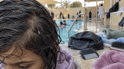 طفل بشعر مبلل قرب مسبح، مع ظهور قملة على الشعر وأدوات فحص وعلاج القمل بجانبه.
